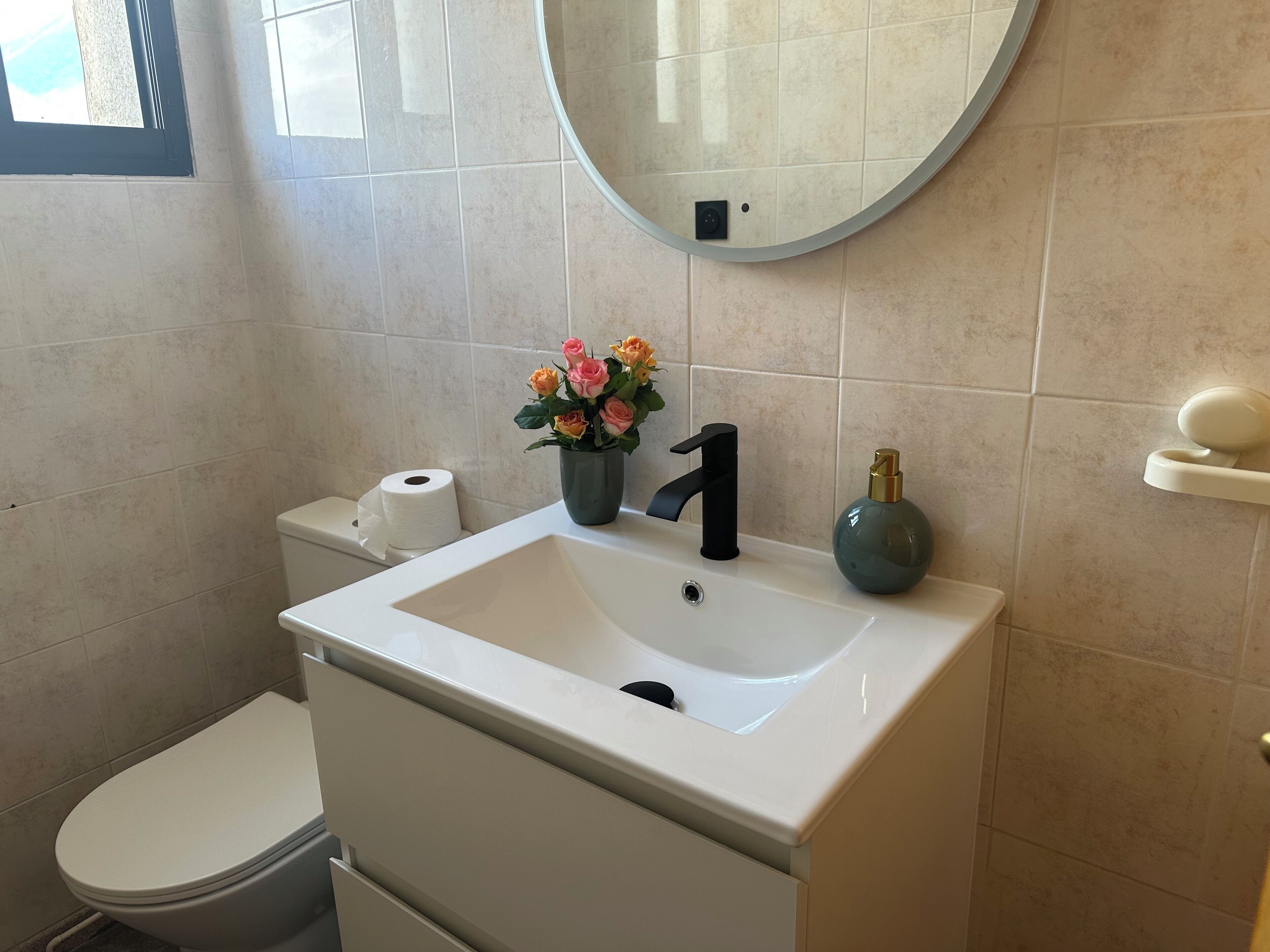 A bathroom with a white sink, a toilet, a mirror, and a vase with flowers.