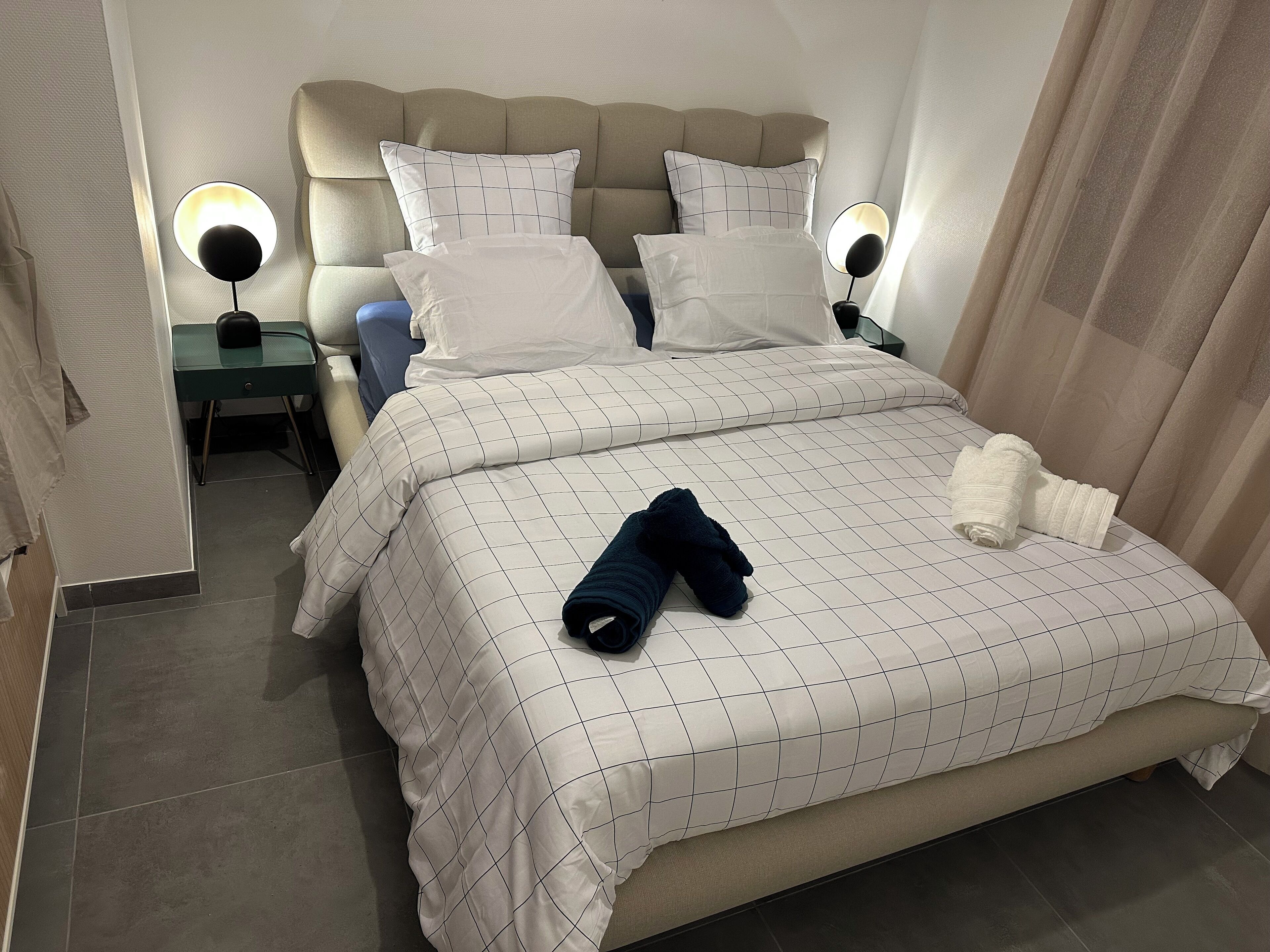 Een net opgemaakt bed met een geruit sprei, twee bedlampen en een hoofdeinde.