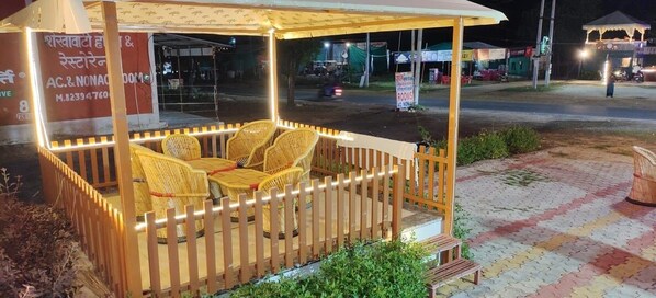 A covered outdoor seating area with wicker furniture and a wooden fence. - Shyam Krapa Hotel (Shri Madhopur)