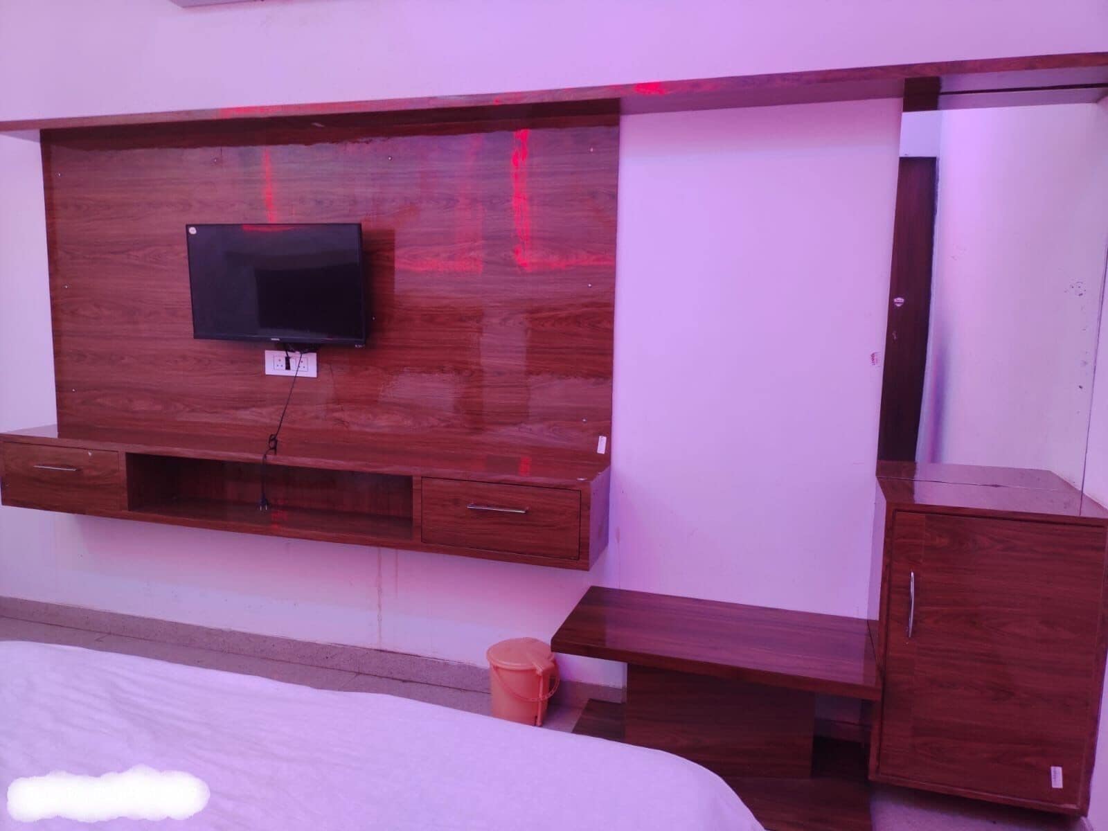 Une chambre à coucher avec une tête de lit en bois, un téléviseur fixé au-dessus d’une console en bois et un petit meuble en bois.