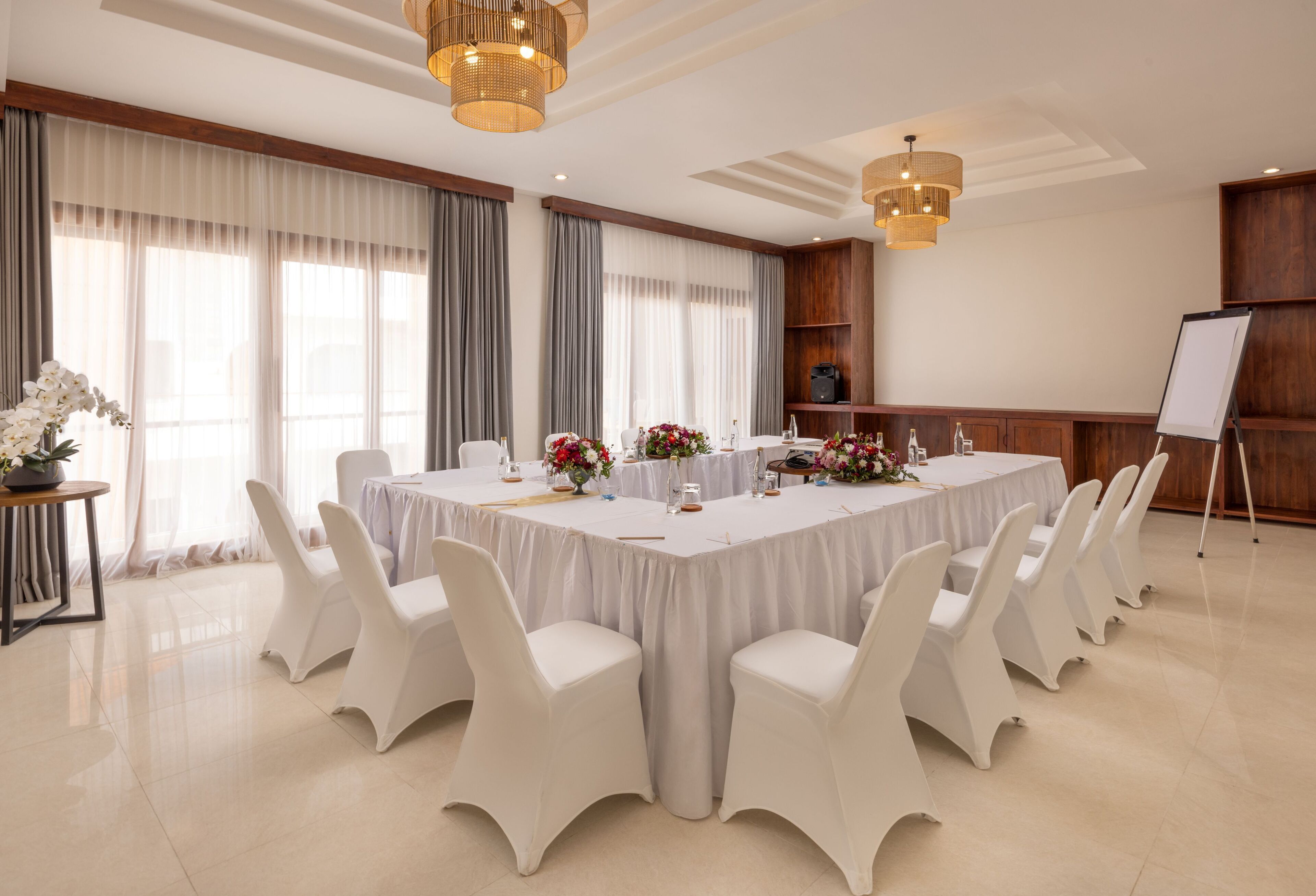 A conference room with a long table, white chairs, and floral centerpieces.