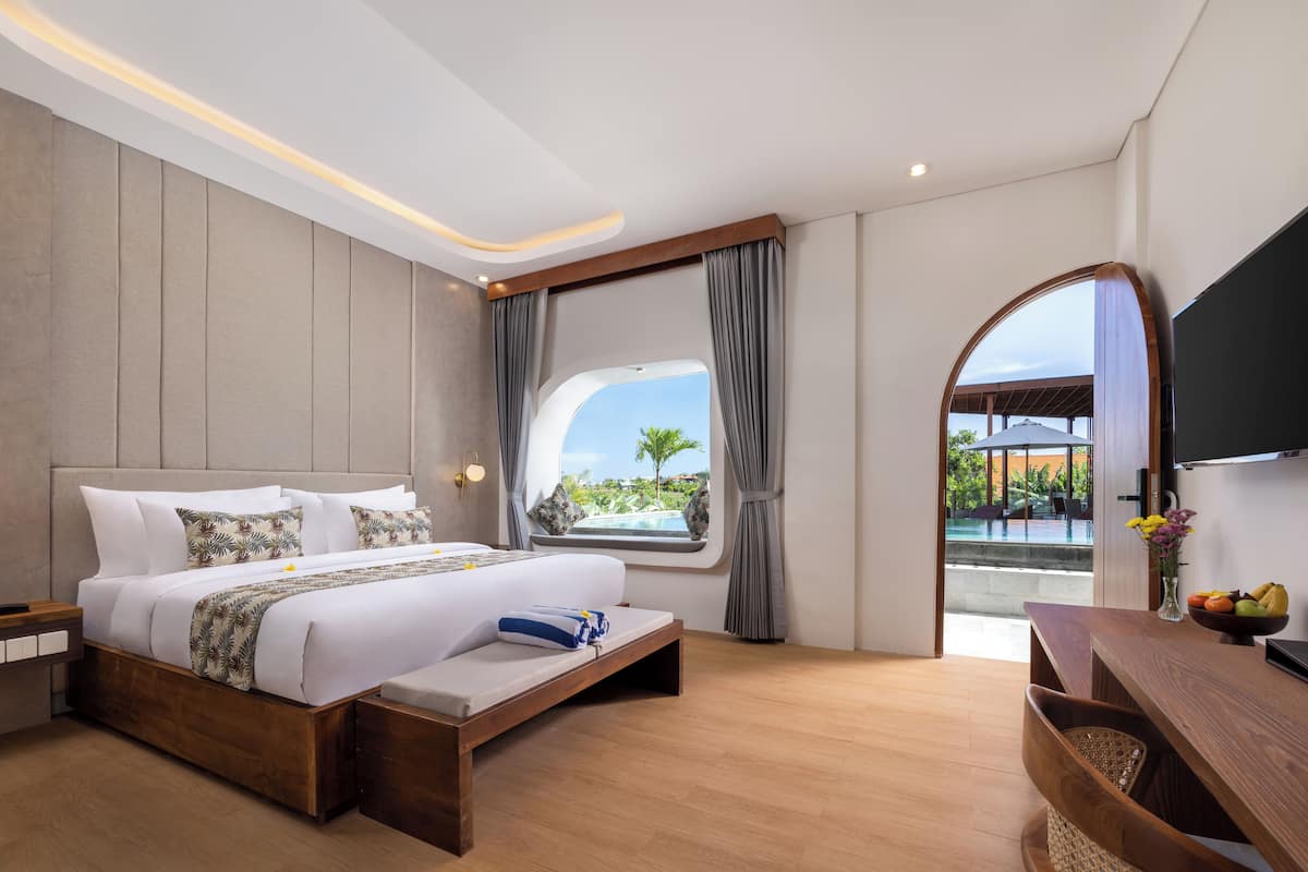 Une chambre d’hôtel moderne avec un grand lit, un banc en bois, une télévision et une vue sur une piscine et des palmiers.