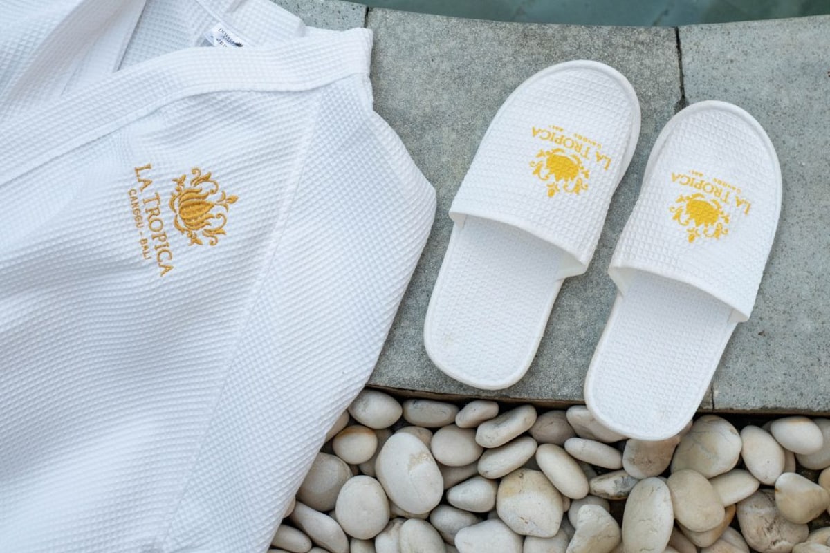 A white shirt and two white slippers with a golden emblem on a stone surface near a pool.