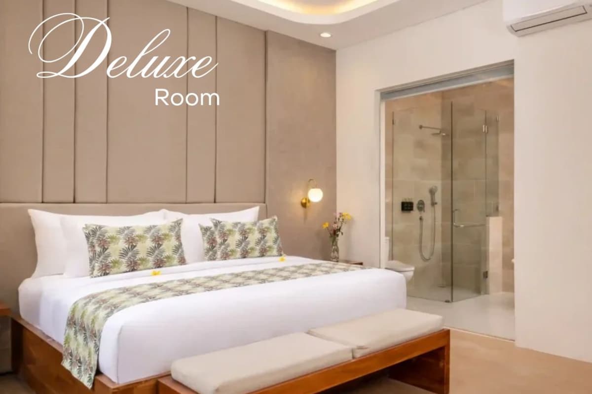 A modern bedroom with a large bed, a bench, a glass shower, and a wall-mounted light.