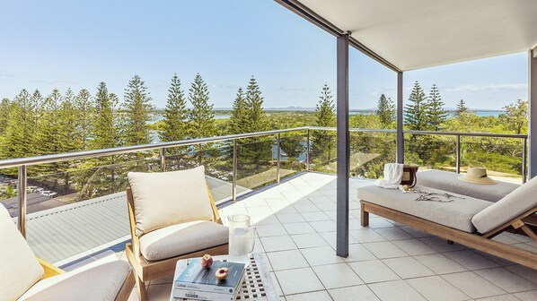 Ein Balkon mit Blick auf Bäume und Wasser, ausgestattet mit zwei Sofas und einem Tisch.