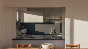 Une cuisine moderne avec des plans de travail sombres, un évier et des placards. On y trouve une table à manger avec des chaises et un saladier posé dessus.