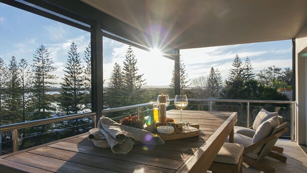 Une terrasse en bois avec une table dressée pour un repas, donnant sur un paysage boisé sous un ciel dégagé.