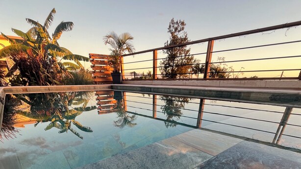 A swimming pool with a tiled deck, surrounded by a metal railing and palm trees. - Furnished bungalow sea view (Saint-Pierre)