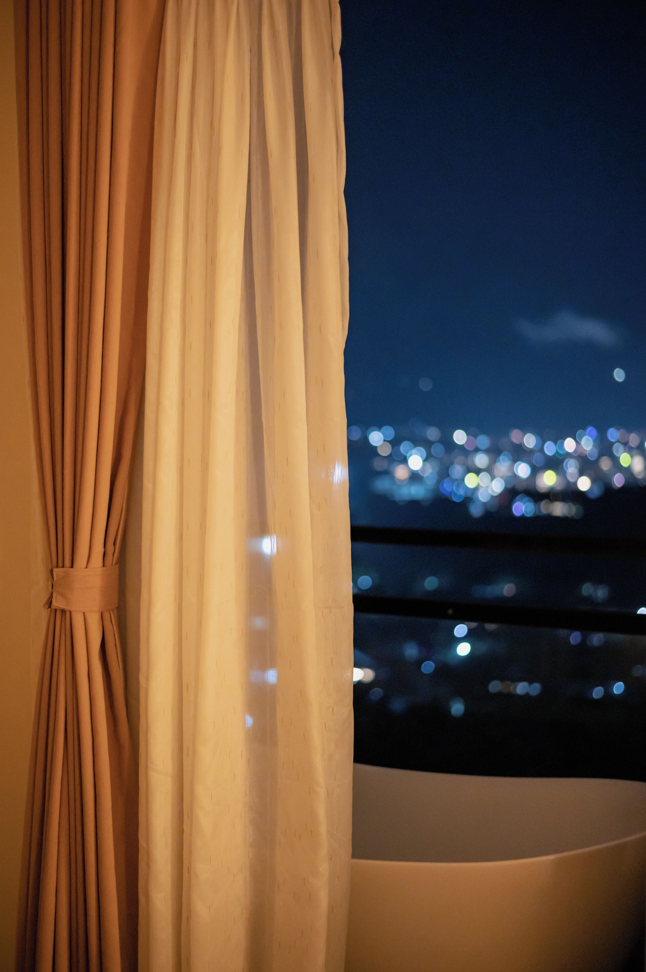 A view of a cityscape at night through a window with curtains.