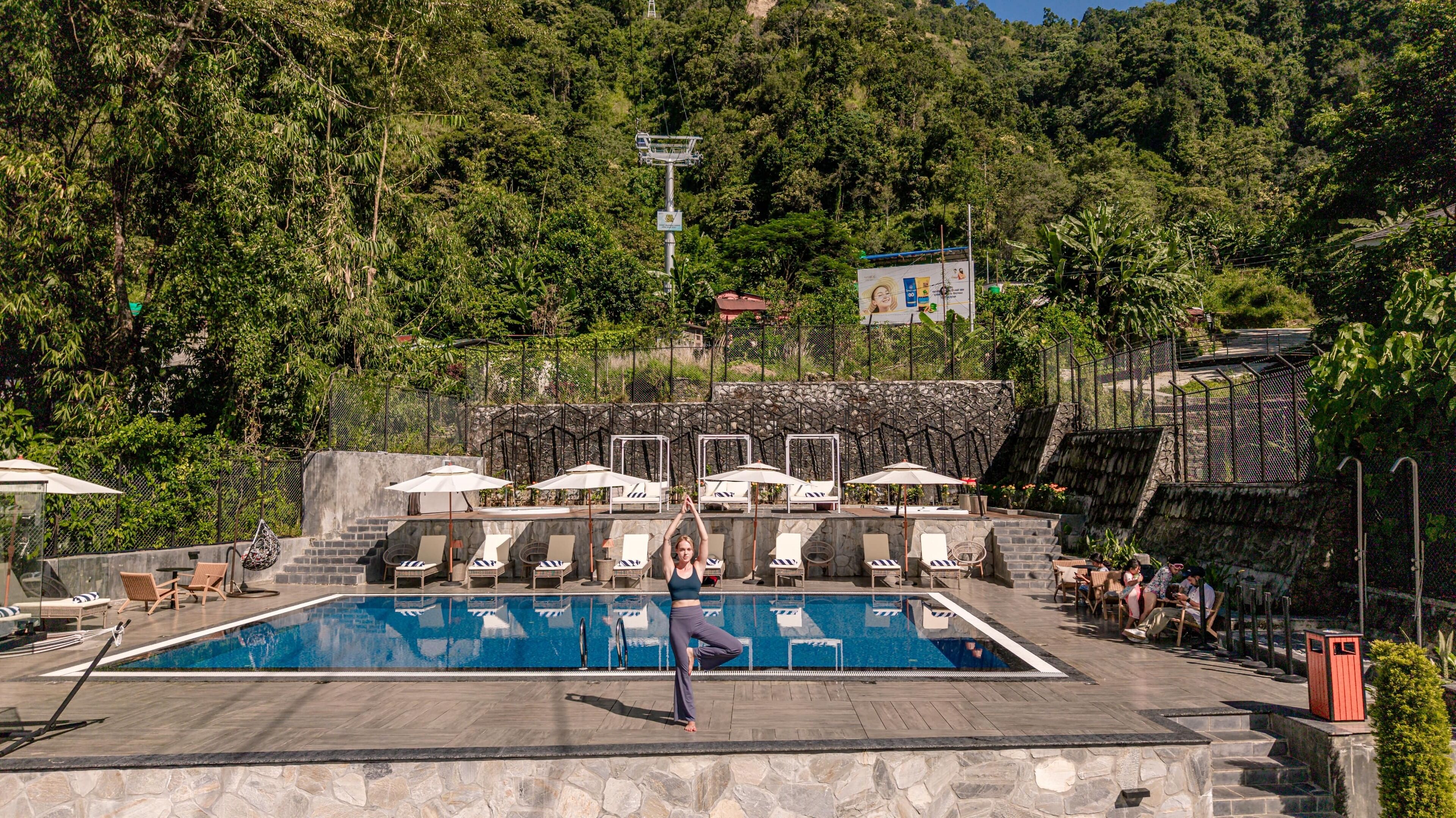 A pool area with lounge chairs and umbrellas, surrounded by stone walls and lush greenery.