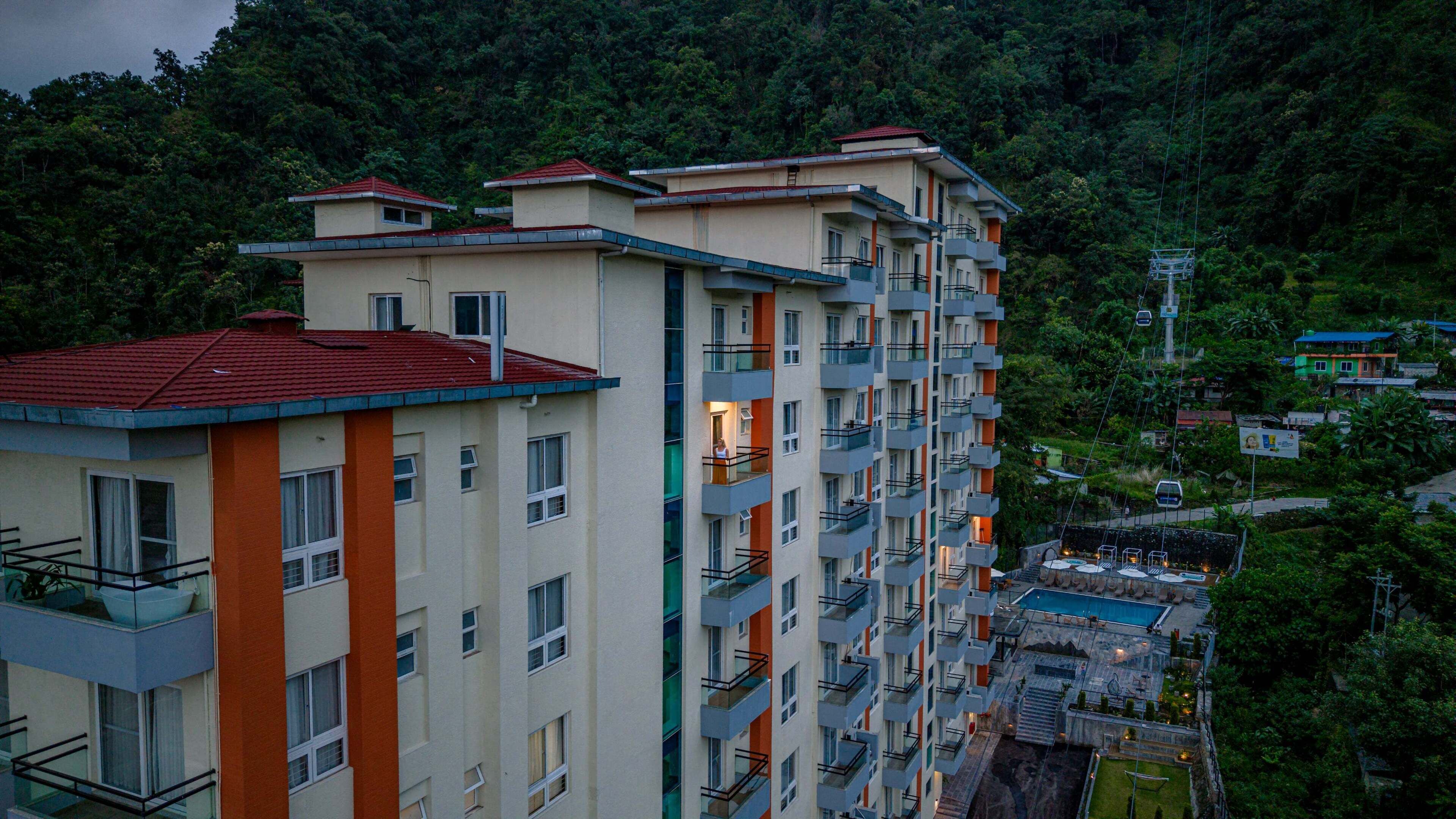 Un hotel de varios pisos con balcones, una piscina y vistas a una ladera boscosa.