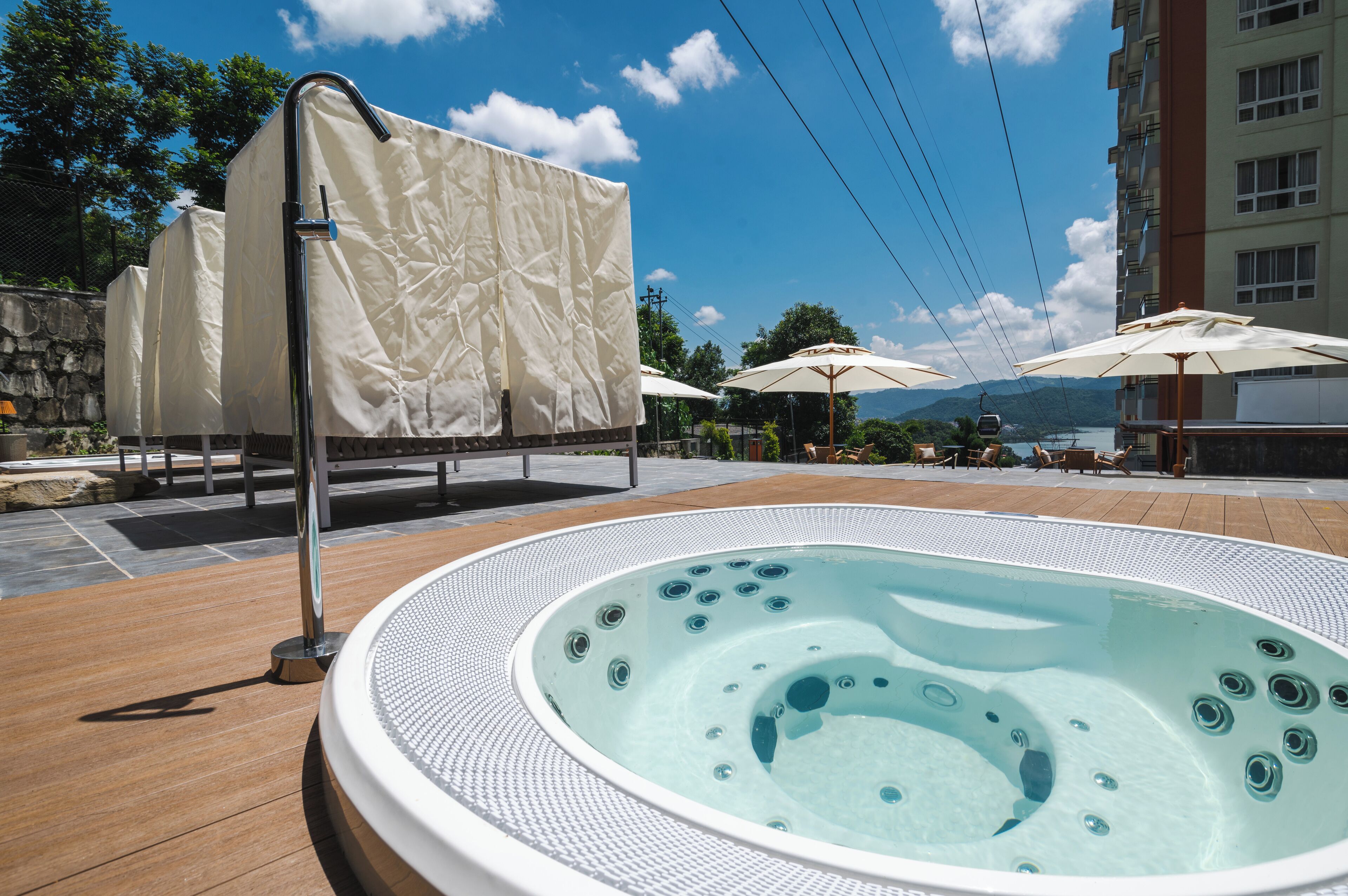 A hot tub with a tiled deck, covered umbrellas, and a stone wall in the background.