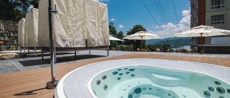 A hot tub with a tiled deck, covered umbrellas, and a stone wall in the background.