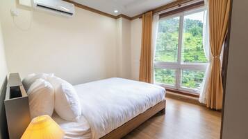 Un dormitorio con cama, aire acondicionado, lámpara y ventana con cortinas.