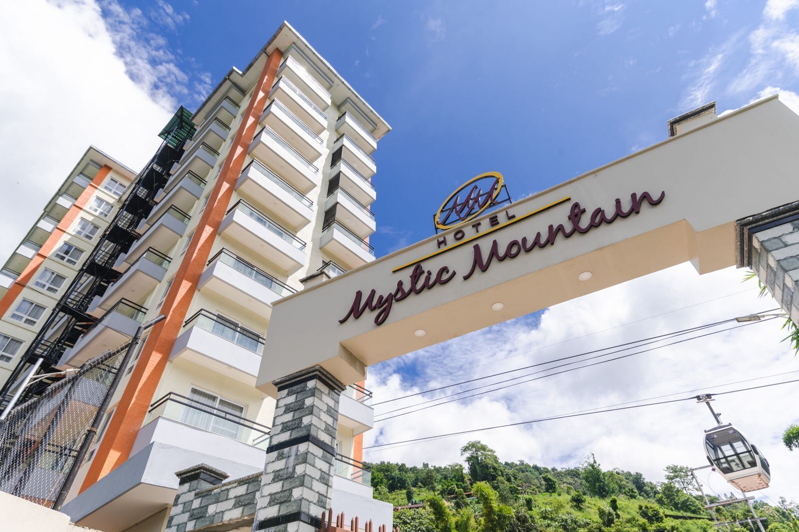 A hotel sign with "Mystic Mountain" written on it, a cable car, and a multi-story building in the background.