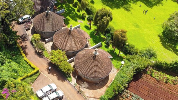 A large, circular building with a tiled roof, surrounded by well-maintained gardens and a few parked vehicles. - Thayu House (Limuru)