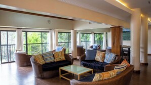 A spacious living area with wicker furniture, large windows, and a view of greenery. - Thayu House (Limuru)