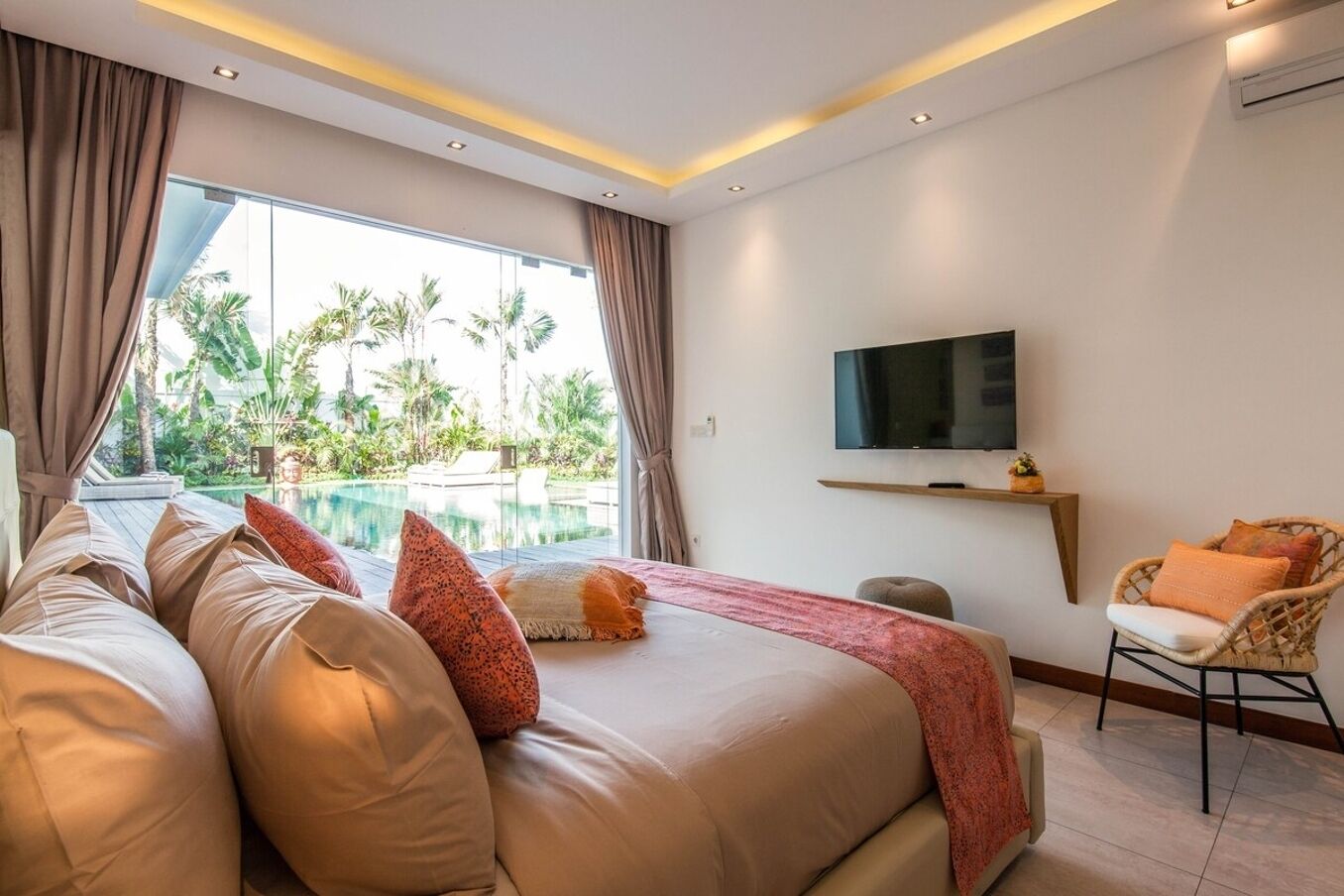Habitación de hotel moderna con una cama grande, televisor, una silla y vistas a una piscina y zonas verdes.