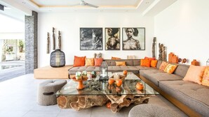 A modern living room with a glass coffee table, a grey sofa, and a large window overlooking a pool. - Stunning 6 Bedroom Villa Only 400m to the Beach (Canggu)