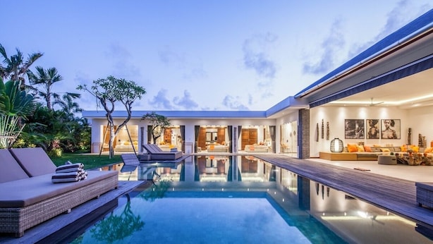 A modern house with a swimming pool, outdoor seating, and a well-lit interior. - Stunning 6 Bedroom Villa Only 400m to the Beach (Canggu)