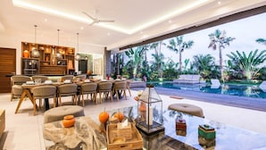 A modern interior with a dining area, a glass table with decorative items, and a view of a pool and tropical plants. - Stunning 6 Bedroom Villa Only 400m to the Beach (Canggu)
