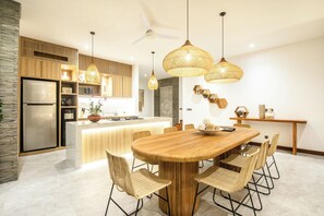 A modern kitchen with a central island, wooden cabinets, and a dining area with wicker chairs. - Seaside Luxury: 4BR Villa, 400m to Finns, Canggu (Canggu)
