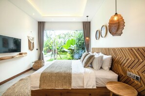 A modern bedroom with a large bed, a TV, and a view of greenery outside. - Seaside Luxury: 4BR Villa, 400m to Finns, Canggu (Canggu)