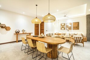 A modern dining area with a wooden table and chairs, pendant lights, and a sofa set in the background. - Seaside Luxury: 4BR Villa, 400m to Finns, Canggu (Canggu)