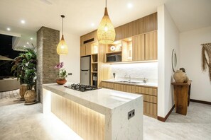 A modern kitchen with a central island, wooden cabinetry, and pendant lighting. - Seaside Luxury: 4BR Villa, 400m to Finns, Canggu (Canggu)