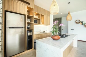 A modern kitchen with wooden cabinetry, a stainless steel refrigerator, a marble countertop, and a potted orchid. - Seaside Luxury: 4BR Villa, 400m to Finns, Canggu (Canggu)