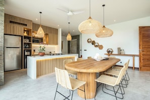 Eine moderne Küche mit Kochinsel, Holzschränken und einem Essbereich mit rundem Tisch und Korbstühlen.
