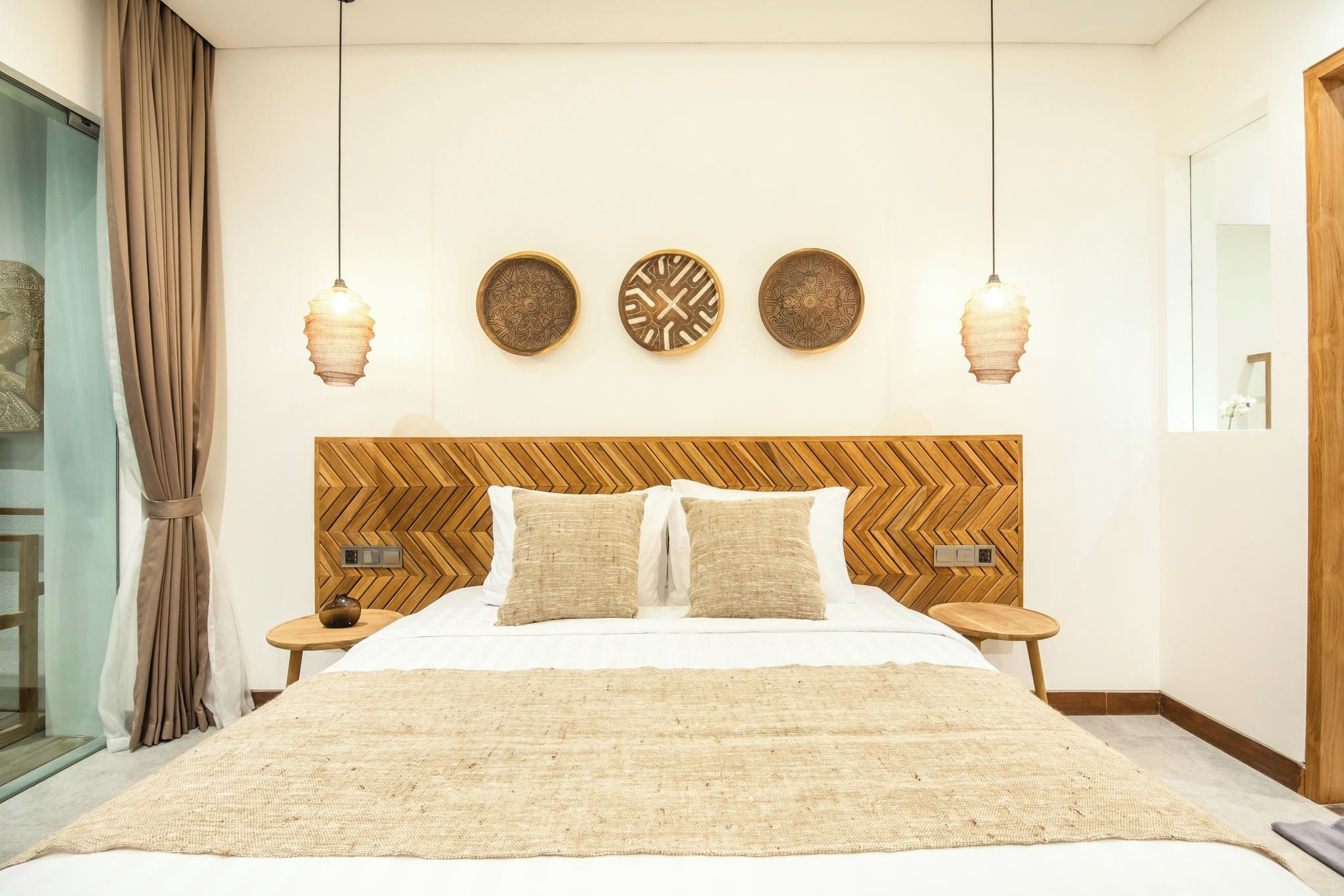 Un dormitorio ordenado con una cama grande, dos mesitas de noche, un cabecero de madera y tres adornos murales.