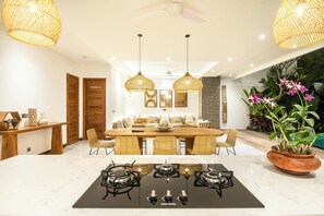 A modern kitchen with a central island, a dining area with a wooden table and chairs, and a potted plant with orchids. - Seaside Luxury: 4BR Villa, 400m to Finns, Canggu (Canggu)