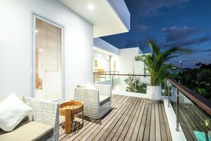 A modern outdoor balcony with a wooden deck, white wicker furniture, and a glass railing overlooking a garden. - Seaside Luxury: 4BR Villa, 400m to Finns, Canggu (Canggu)