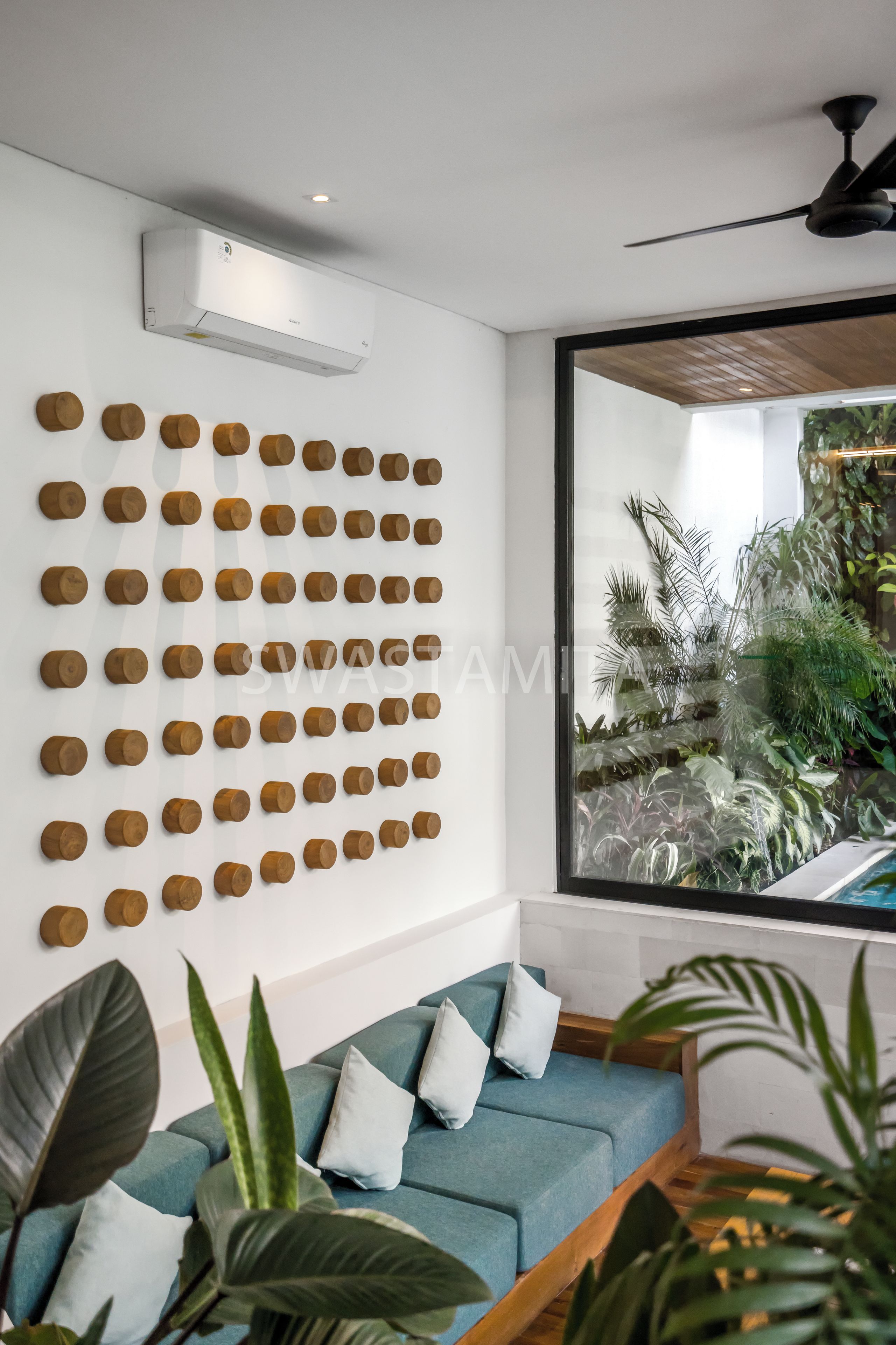 Ein modernes Zimmer mit einem blauen Sofa, einer an der Wand befestigten Holzdeko und einem großen Fenster mit Blick auf einen Garten.