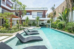 Un espace piscine moderne avec des chaises longues, une clôture en bois et une végétation luxuriante.