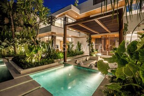 Un espace piscine moderne avec une piscine à eau claire, des plantes environnantes et une pergola en bois.
