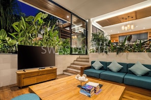 A modern living room with a large TV, wooden coffee table, and a sofa with cushions. There is a staircase leading to another level. - Brand new Luxury 5 br Villa 200m to Brawah Beach (Canggu)