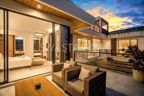 A modern, open-plan living area with a large sliding glass door leading to a bedroom, a balcony with outdoor seating, and a view of the sky. - Brand new Luxury 5 br Villa 200m to Brawah Beach (Canggu)
