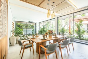 A modern dining area with a large wooden table, grey upholstered chairs, and hanging pendant lights. - Brand new Luxury 5 br Villa 200m to Brawah Beach (Canggu)