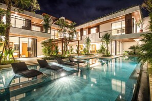 Un hôtel moderne doté d’un espace piscine, comprenant des chaises longues et un intérieur bien éclairé.