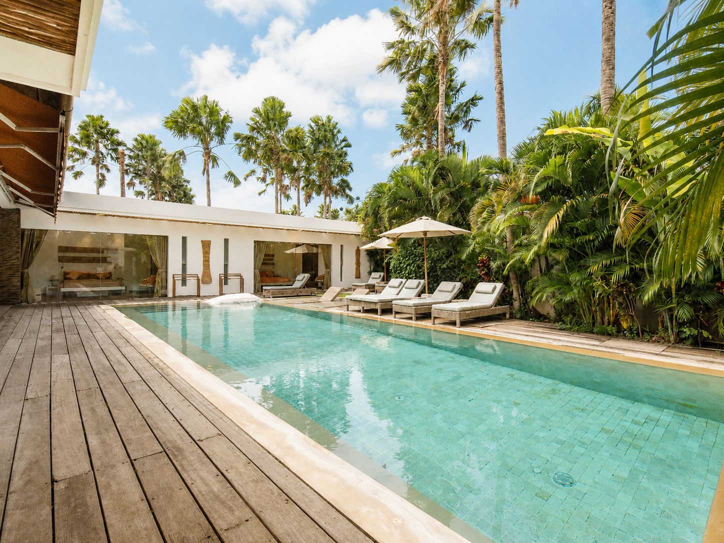 A pool with lounge chairs, surrounded by palm trees and a wooden deck.