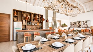 A modern kitchen with wooden cabinetry, a central island, and a dining area with a long table set for six. - Luxurious 5BR Dream Villa, 200m to Berawa Beach (Canggu)