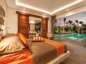 A modern bedroom with a large bed, a vanity, and a view of an outdoor pool. - Luxurious 5BR Dream Villa, 200m to Berawa Beach (Canggu)