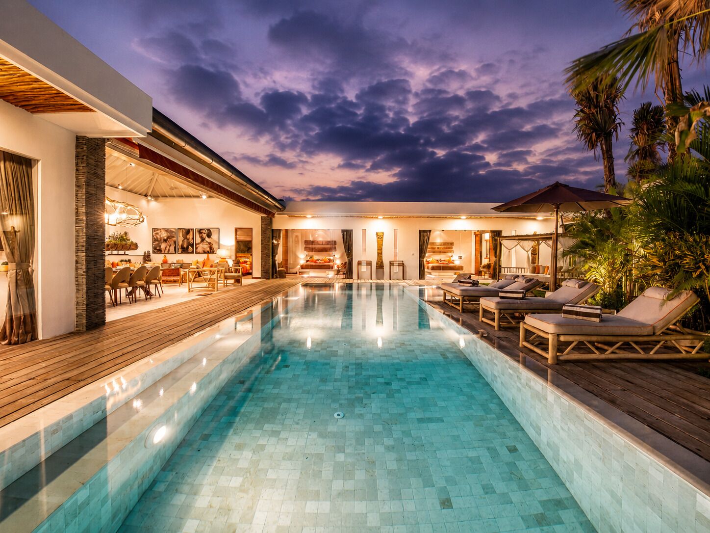A modern pool area with a wooden deck, lounge chairs, and a view of the sky.