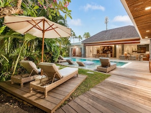 A poolside area with lounge chairs, a wooden deck, and a building with a stone facade.