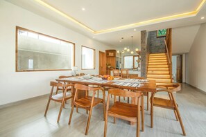 A spacious dining area with a long wooden table and chairs, a large window, and a staircase with wooden steps.