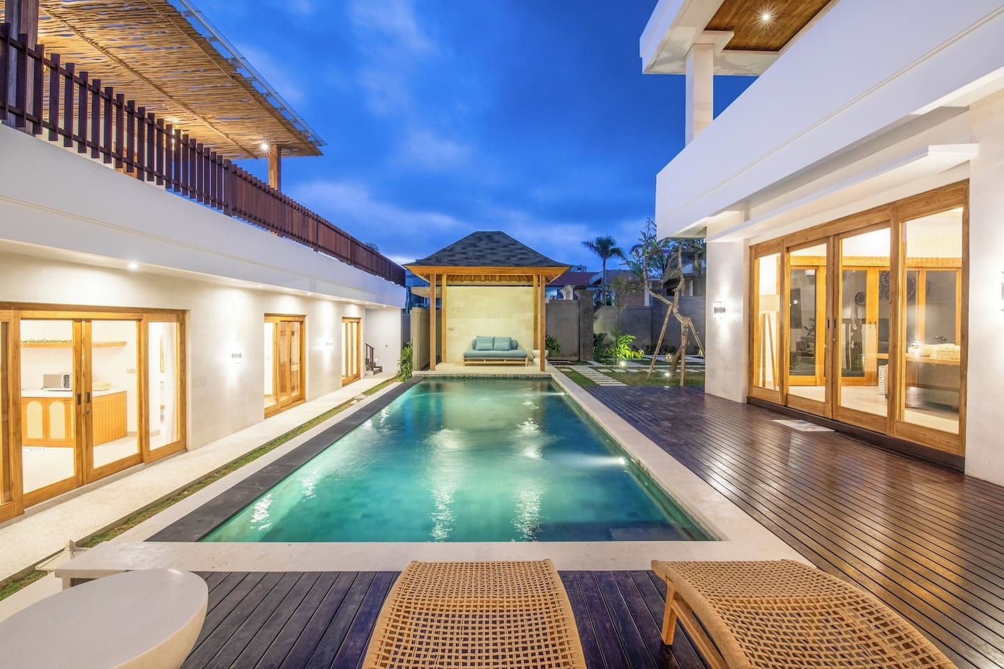 A modern pool area with a wooden deck, a lounge chair, and a covered seating area.
