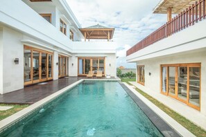 Une maison moderne dotée d’une piscine centrale, de grandes portes-fenêtres coulissantes et d’un patio couvert.