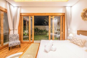 Une chambre avec un grand lit, une chaise, une table de chevet et une vue sur un jardin la nuit.